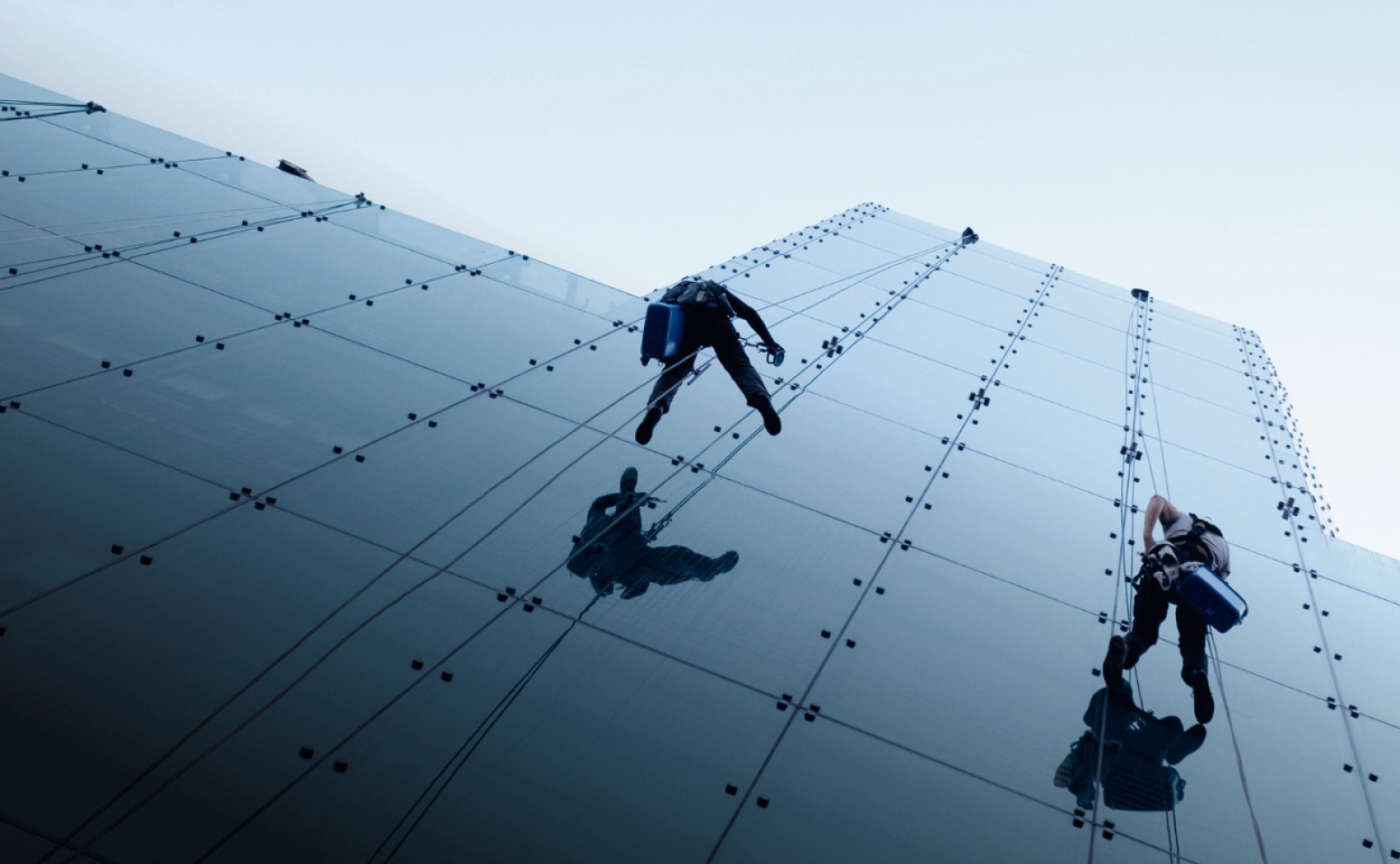 Rope-access technicians descending a blue glass curtain wall