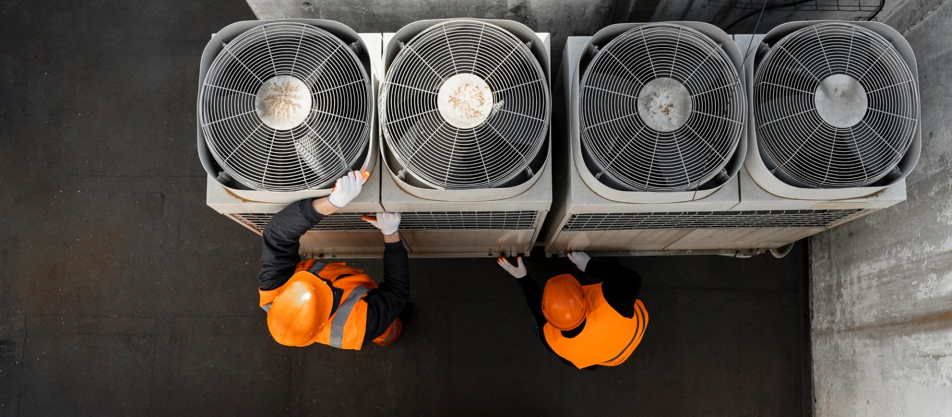 Two technicians in hard hats servicing a bank of rooftop condenser units